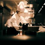 A chef wearing a uniform works diligently in a bustling Japanese restaurant kitchen in Osaka, Japan.