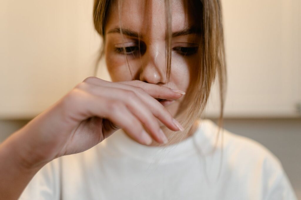 A woman appears deep in thought, with hand over lips, conveying emotional distress.